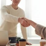 Close-up of professionals shaking hands over coffee in a modern office.