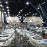 Large indoor temporary medical station with rows of prepared hospital beds and supplies.