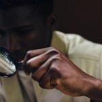 A man closely inspects an object using a magnifying glass.